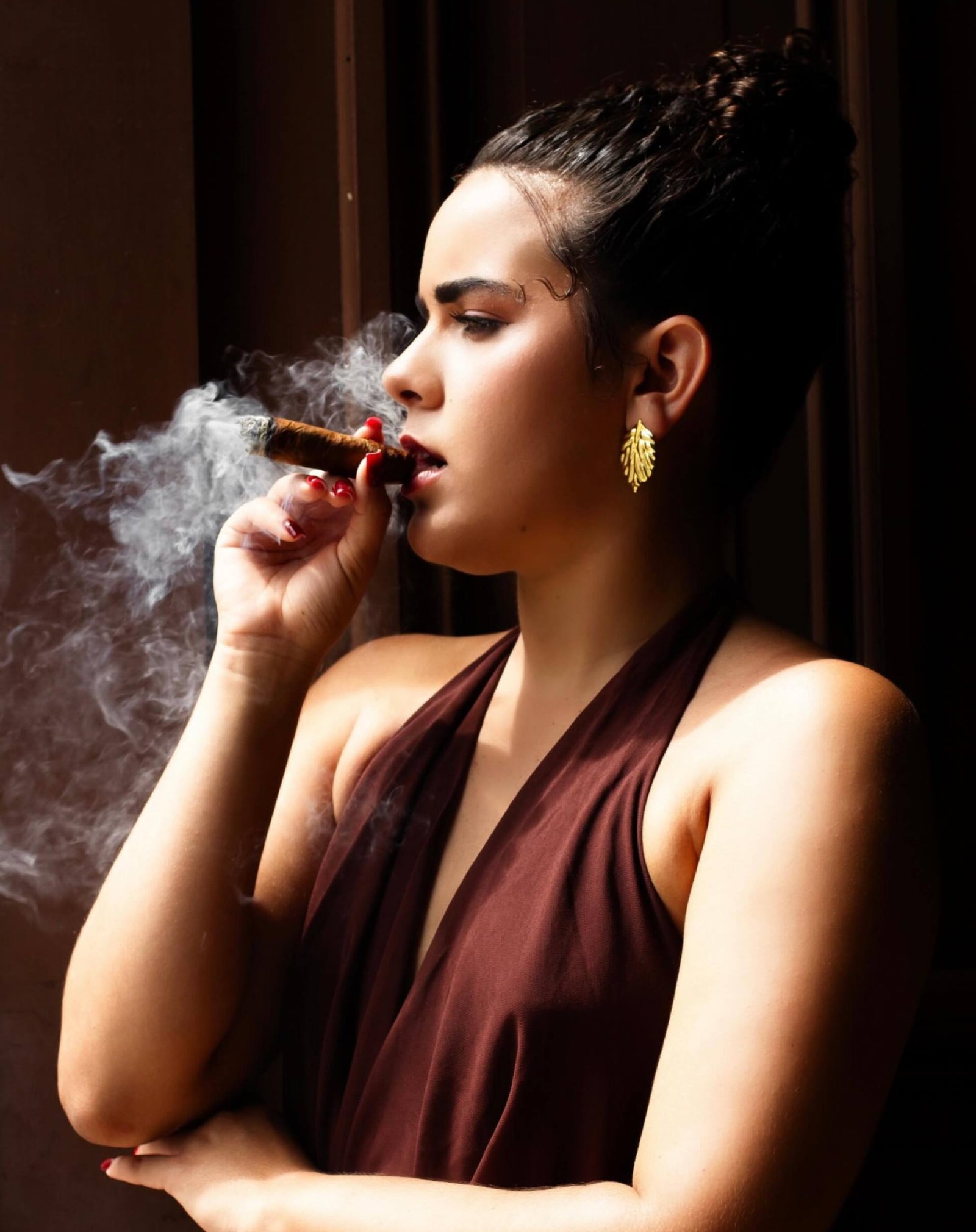 Retrato editorial de mujer de perfil fumando un habano, luz dramática
