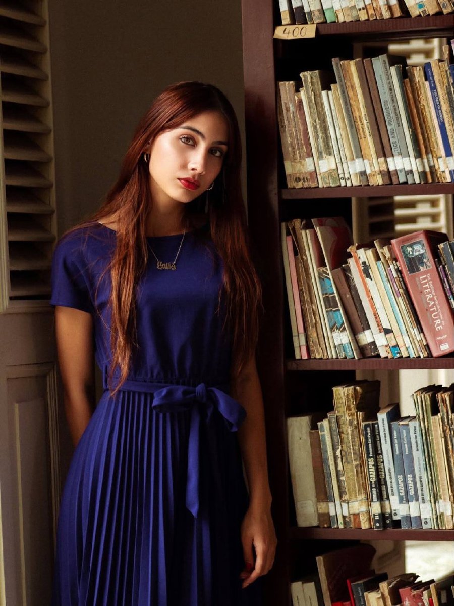 Retrato editorial de mujer con vestido azul junto a una biblioteca